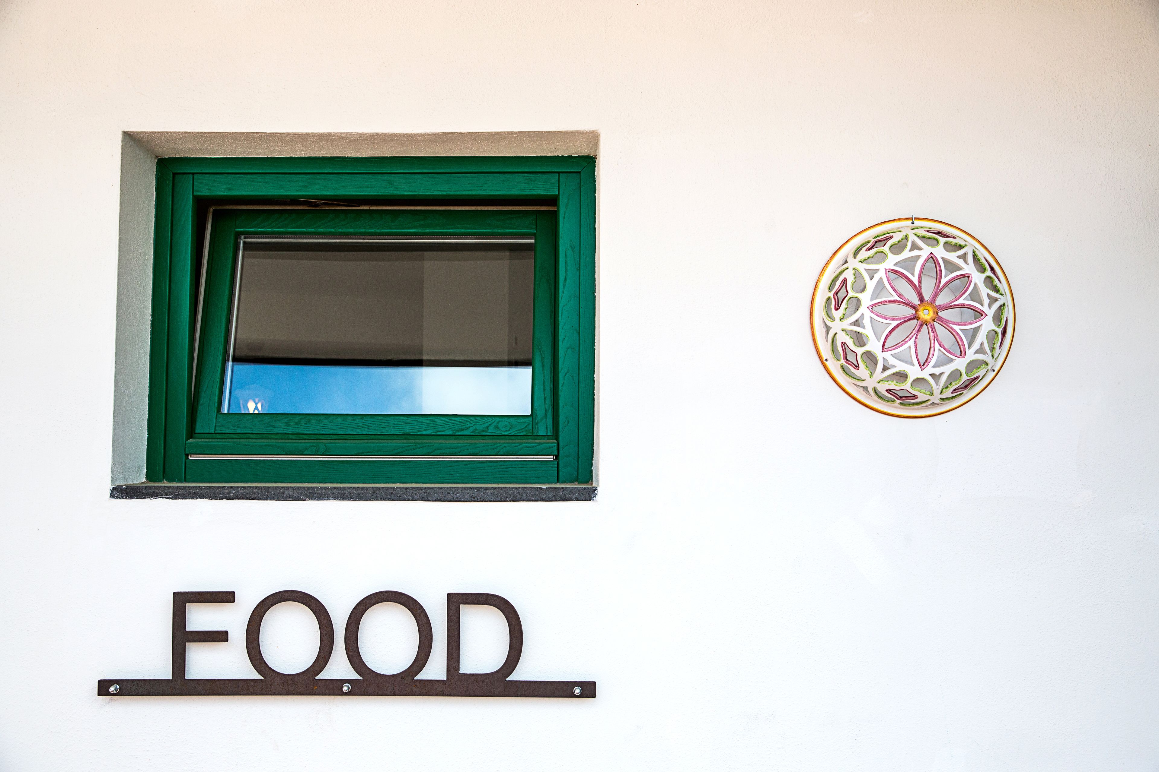 A window with a green frame and a decorative circular piece on the wall.