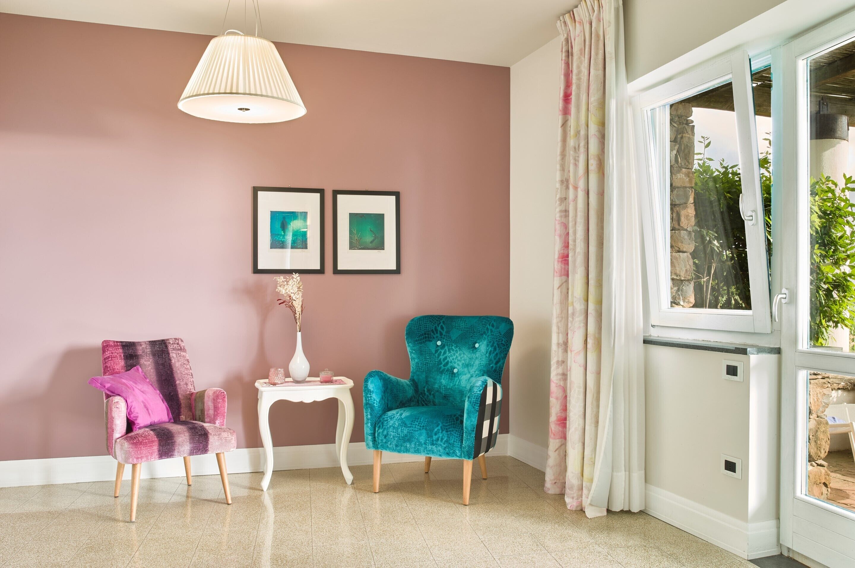 Una habitación con dos sillones, una mesita y una lámpara colgante. Hay dos cuadros en la pared.