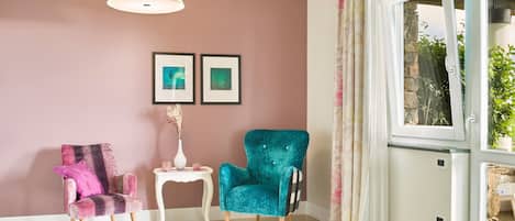 Una habitación con dos sillones, una mesita y una lámpara colgante. Hay dos cuadros en la pared.
