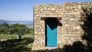 Un edificio in pietra con una porta blu, immerso nel verde e con vista sul mare.