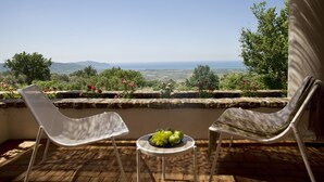 Une terrasse avec deux chaises blanches, une petite table sur laquelle se trouve un saladier rempli de pommes vertes, et une vue sur le paysage.