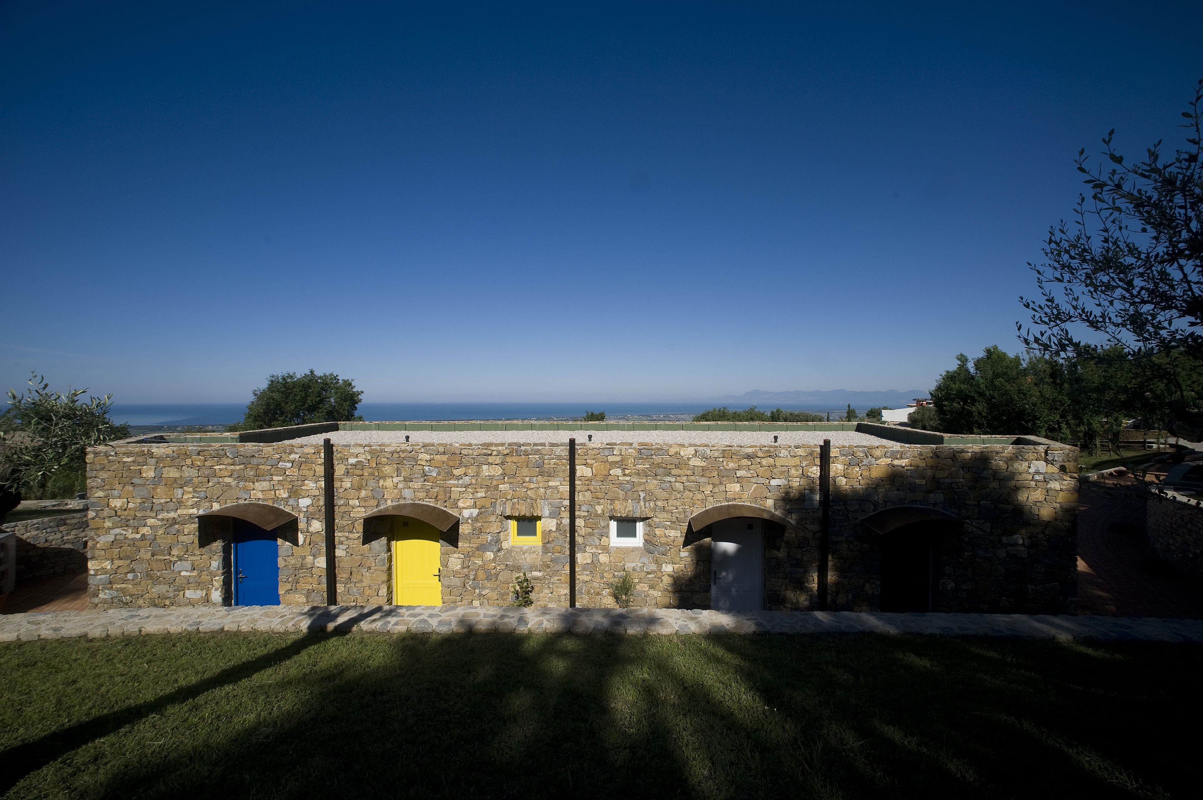 Un edificio de piedra con varias puertas, incluyendo una azul y una amarilla, y vista al mar de fondo.