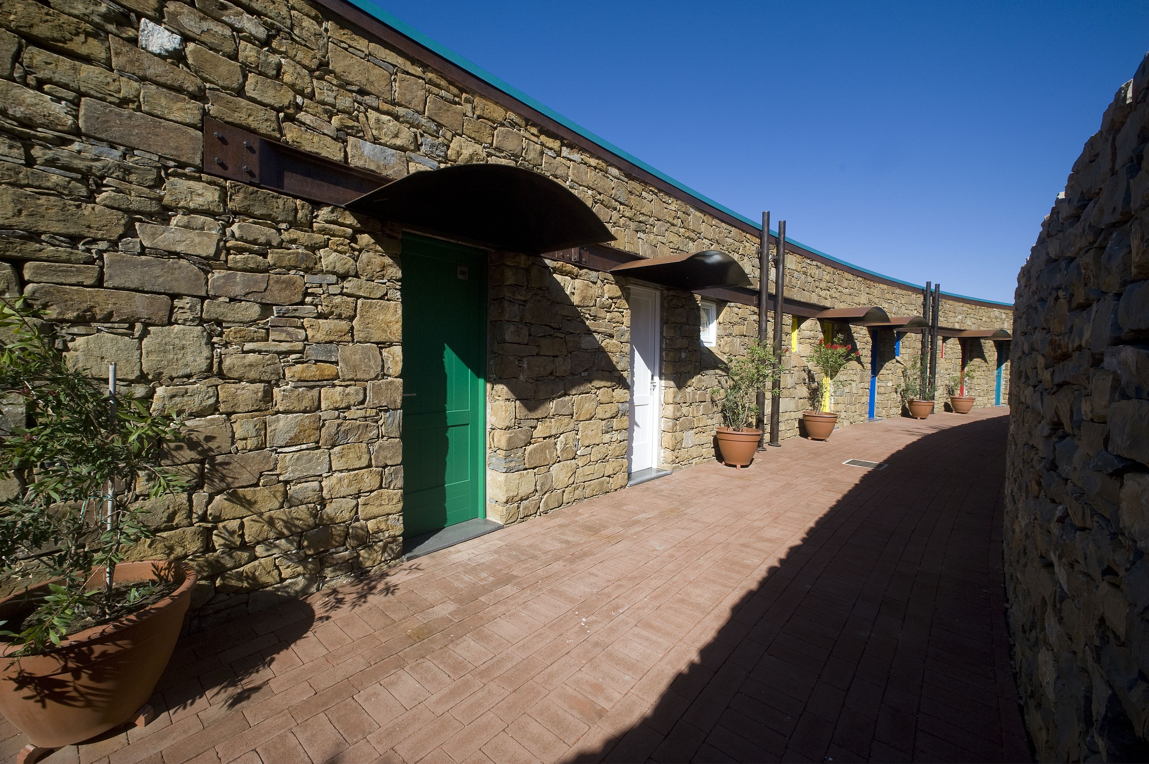 A stone building with a brick pathway, green doors, and potted plants.
