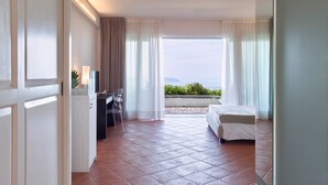 Une chambre d’hôtel avec un lit, un bureau et une chaise, une télévision et une vue sur la mer.