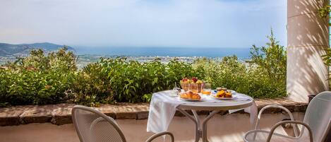 A table set for breakfast with a view of the sea and hills.