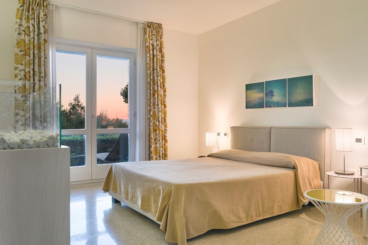 Een hotelkamer met een bed, een glazen tafel, een lamp en een schilderij aan de muur.
