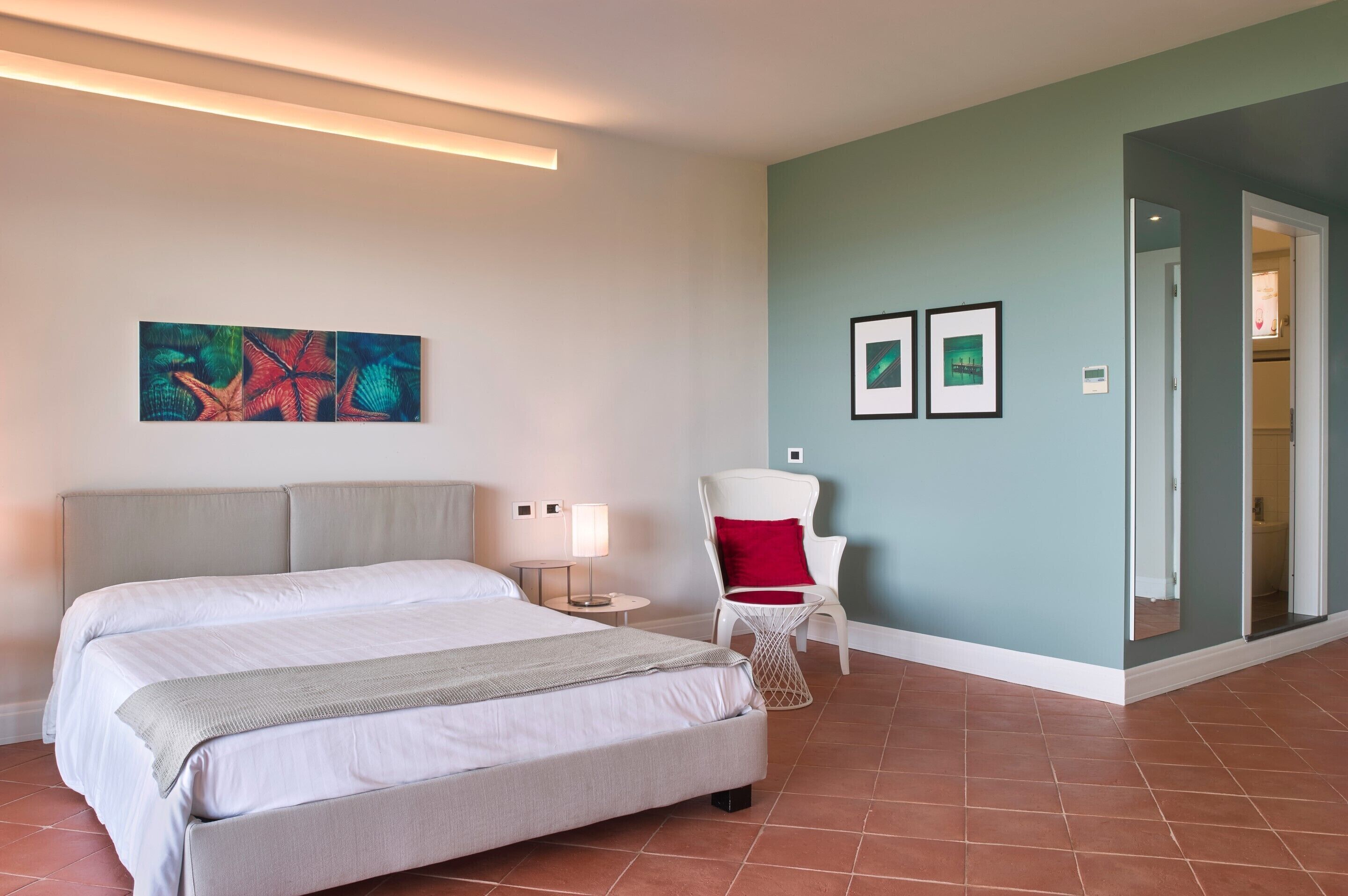 Una habitación de hotel con una cama grande, una silla, una mesita de noche y obras de arte en la pared.