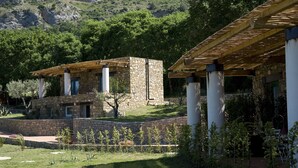 Un bâtiment en pierre doté d’une pergola en bois, entouré d’un mur de pierre et d’une végétation luxuriante.