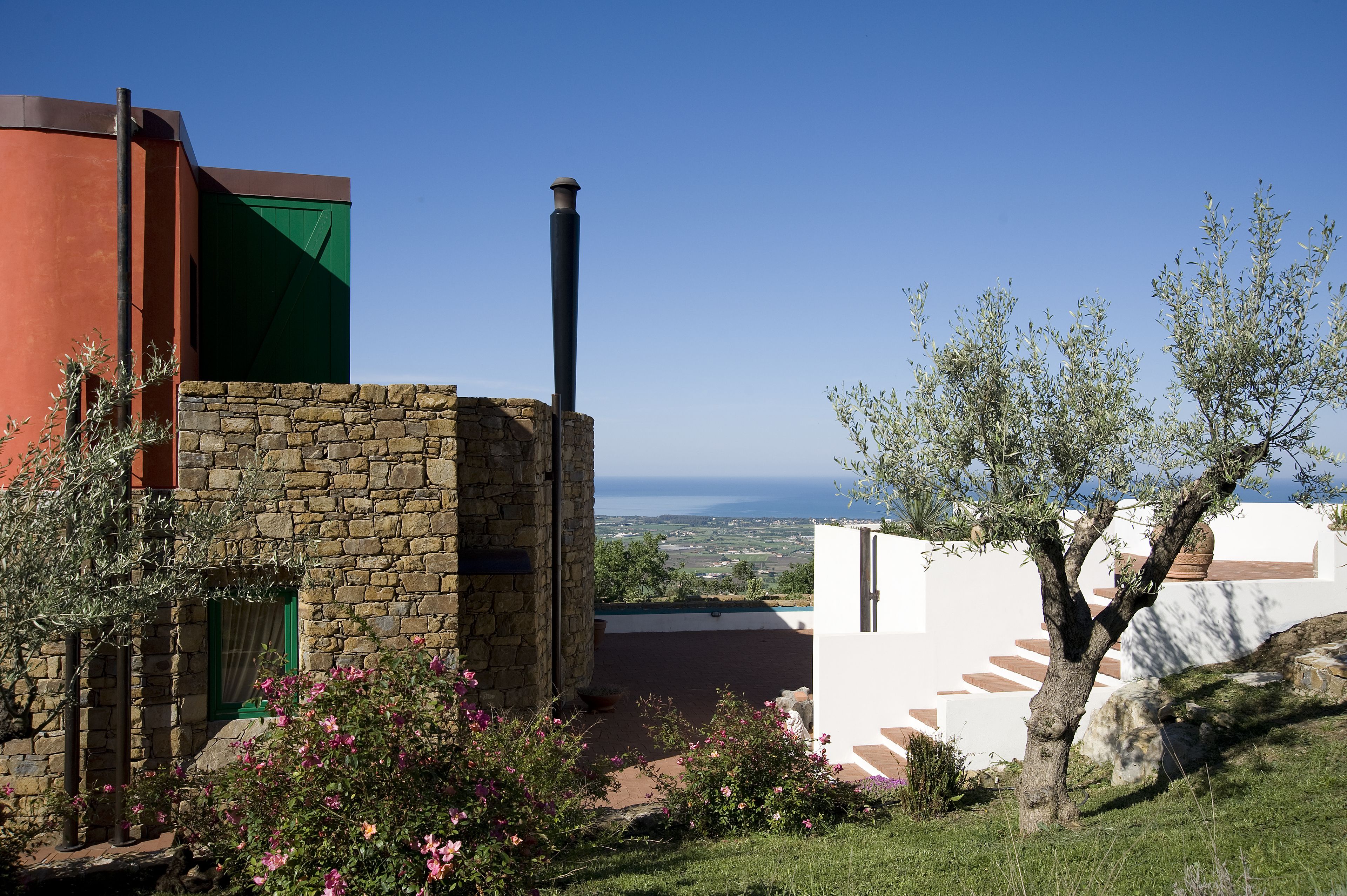 A stone building with a green window, a chimney, and a view of the sea.