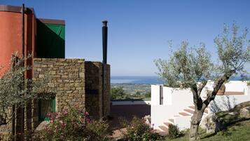 A stone building with a green window, a chimney, and a view of the sea.