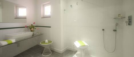 A modern bathroom with a glass-enclosed shower, a sink with a green towel, and a vase with flowers.