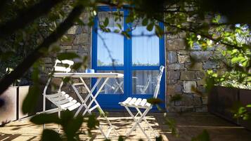 Une terrasse avec un mur en pierre, une porte bleue et des chaises pliantes blanches.