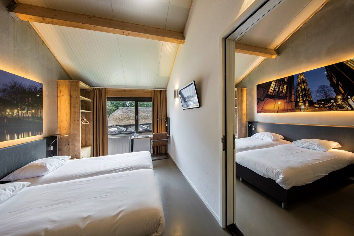 Ein modernes Hotelzimmer mit zwei Betten, einem Schreibtisch und einem großen Fenster mit Blick auf die Stadt.