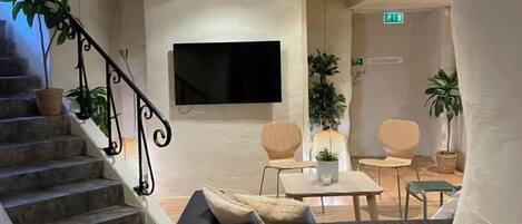 A lobby with a staircase, a flat-screen TV, seating area, and potted plants.