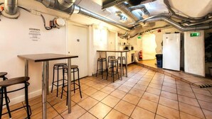 A kitchen with a bar area, including stools and a counter. There are visible pipes and a fire extinguisher. - Nomad Cave (Stockholm)