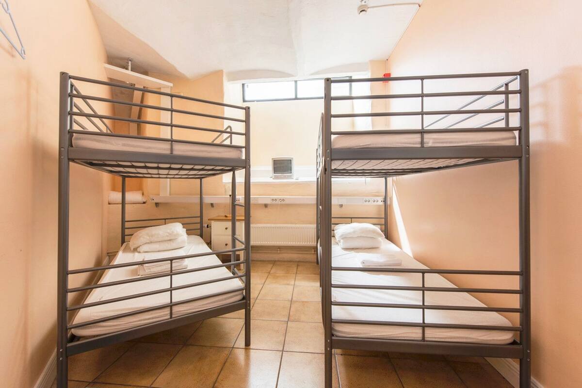 A dormitory room with bunk beds, a small desk, and a radiator.