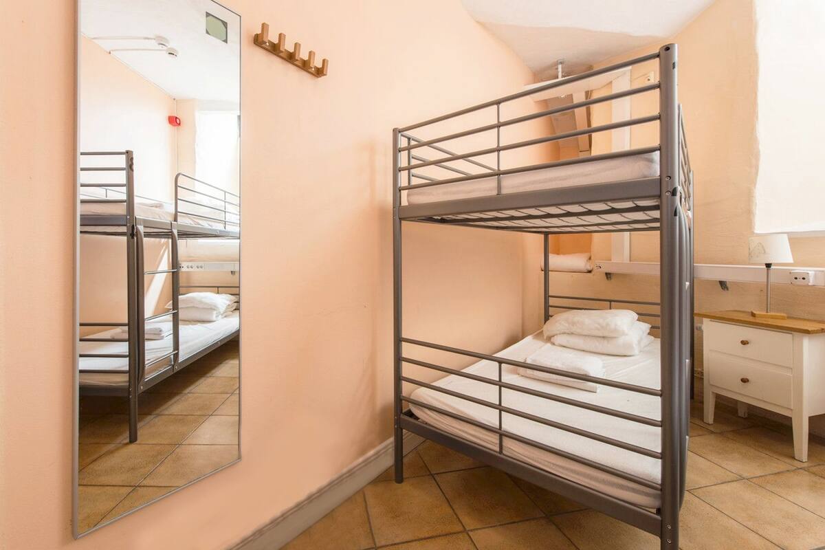 A bunk bed room with a mirror, a bedside table, and a dresser.