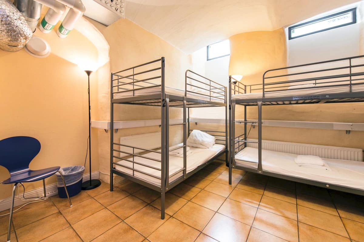 A dormitory room with bunk beds, a chair, a trash bin, and a lamp.