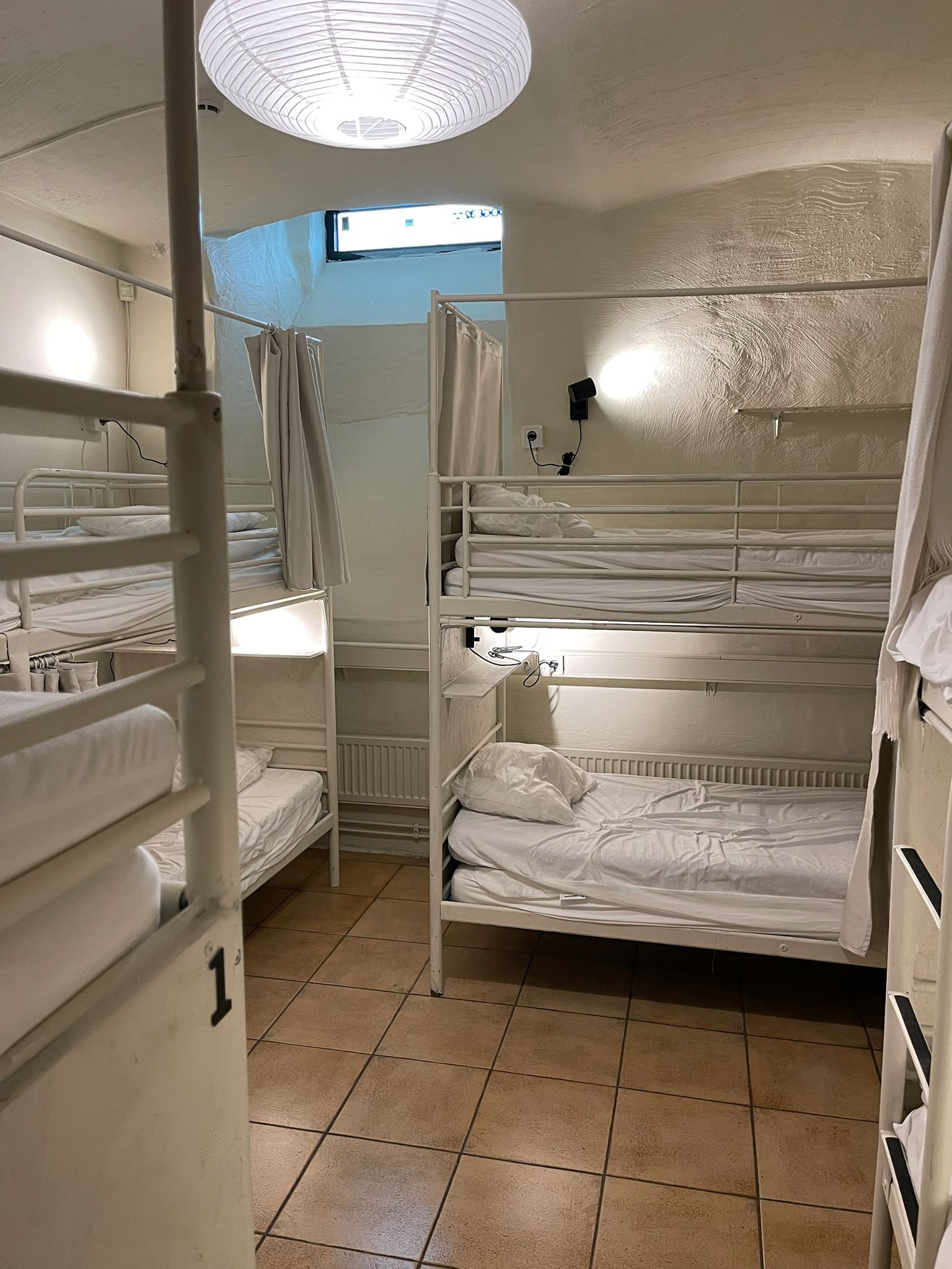 A bunk room with multiple beds, a window, and a ceiling light fixture.