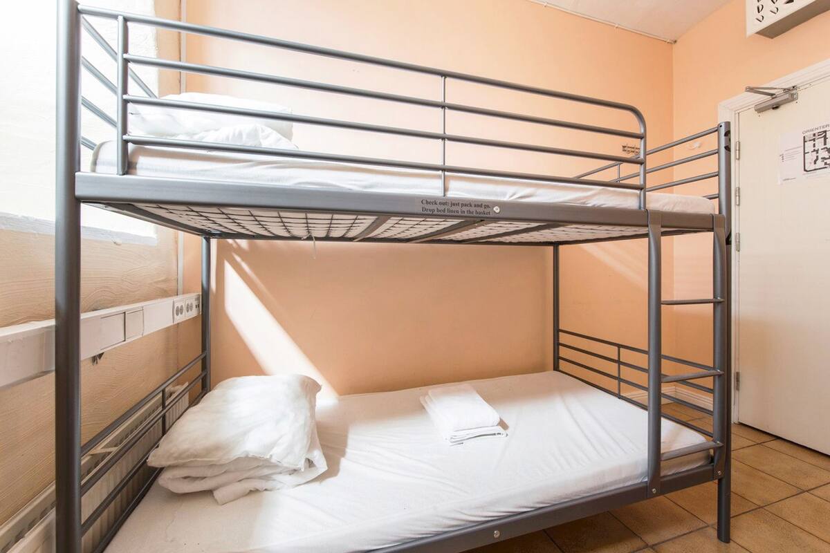 A bunk bed with a mattress and pillows, a metal railing, and a door with a sign.