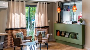 Ein moderner Empfangsbereich mit einem grünen Tresen, zwei Sesseln, einem kleinen Tisch und Blick ins Grüne durch die Fenster.
