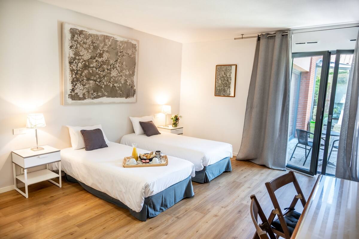 A hotel room with two beds, a dining table, and a balcony with a view.