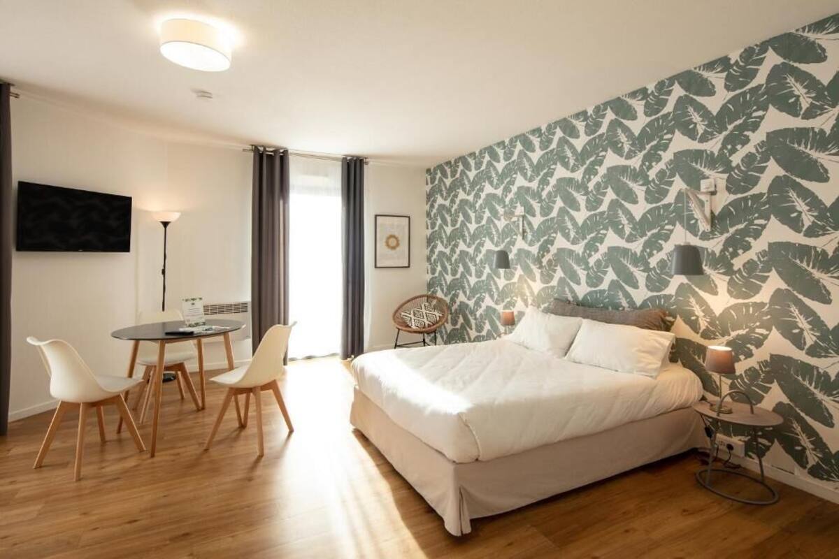 A bedroom with a bed, a dining table with chairs, a TV, and a patterned wall.