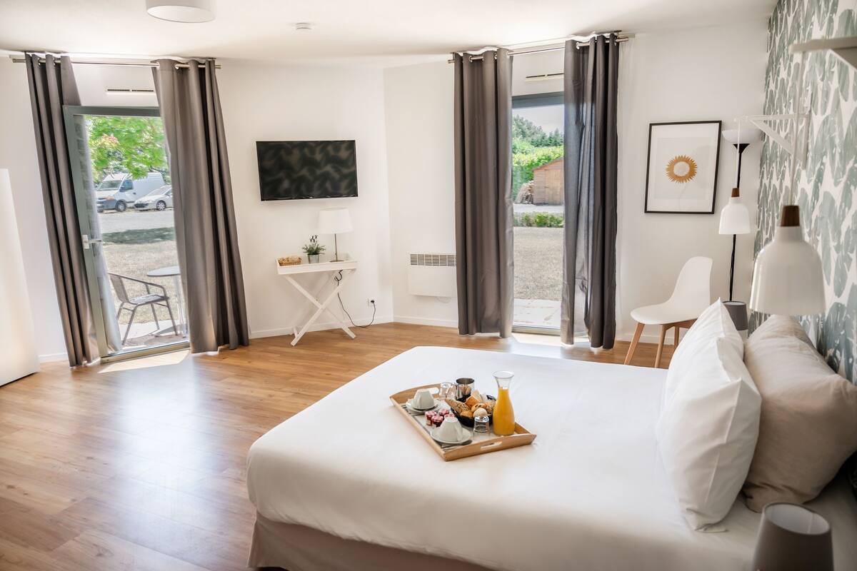 A hotel room with a large bed, breakfast tray, a TV, a desk, and a view of the outside.