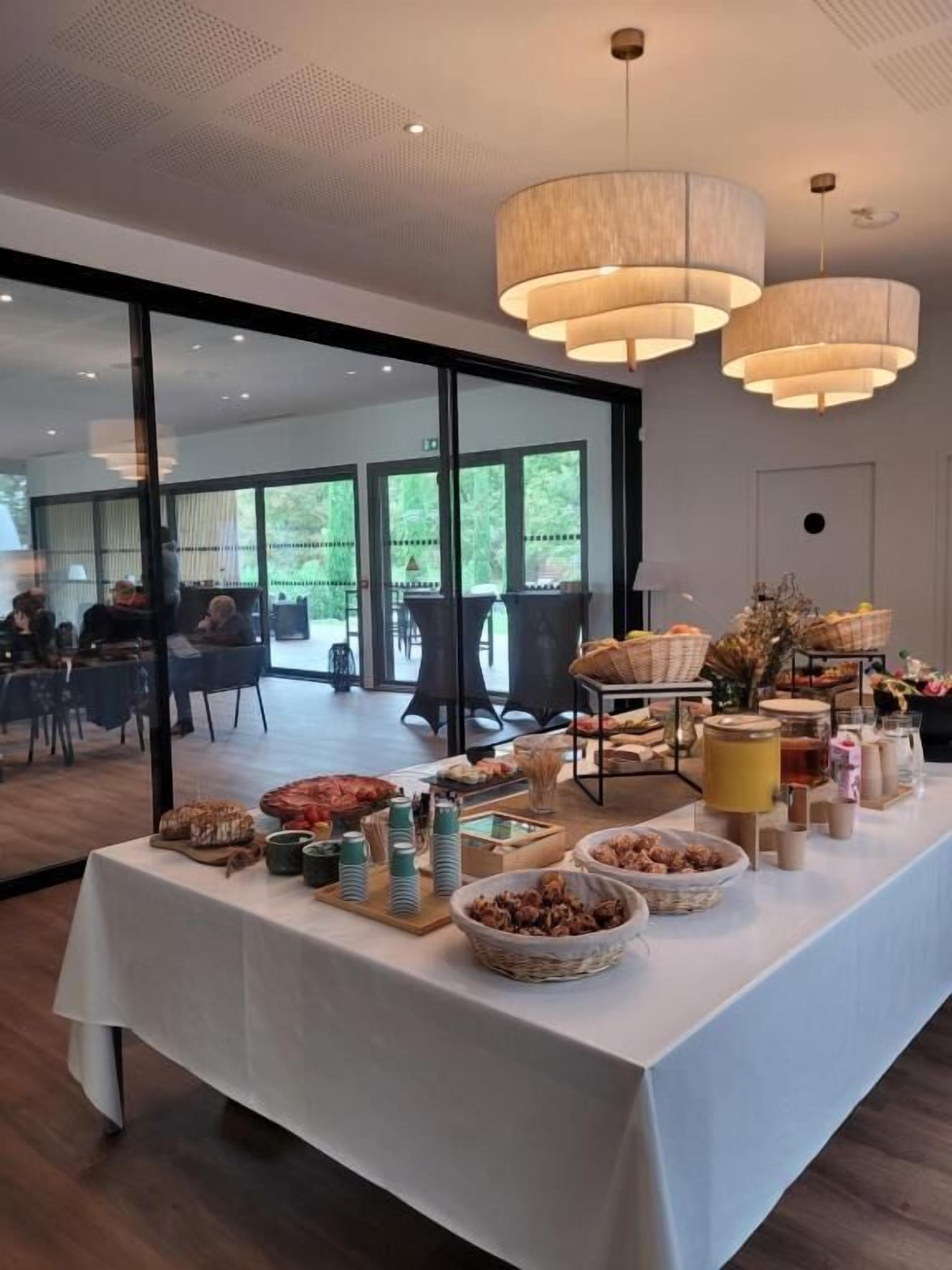 A buffet table with various food items and beverages, set in a room with large windows and modern lighting fixtures.