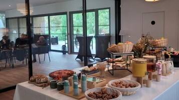 A buffet table with various food items and beverages, set in a room with large windows and modern lighting fixtures.
