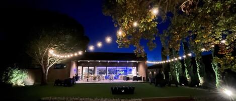 An outdoor dining area with string lights, a covered seating area, and a view of the building's interior.