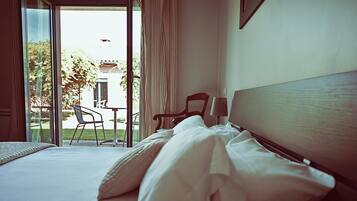 A hotel room with a bed, a chair, and a table near a sliding glass door leading to an outdoor area.