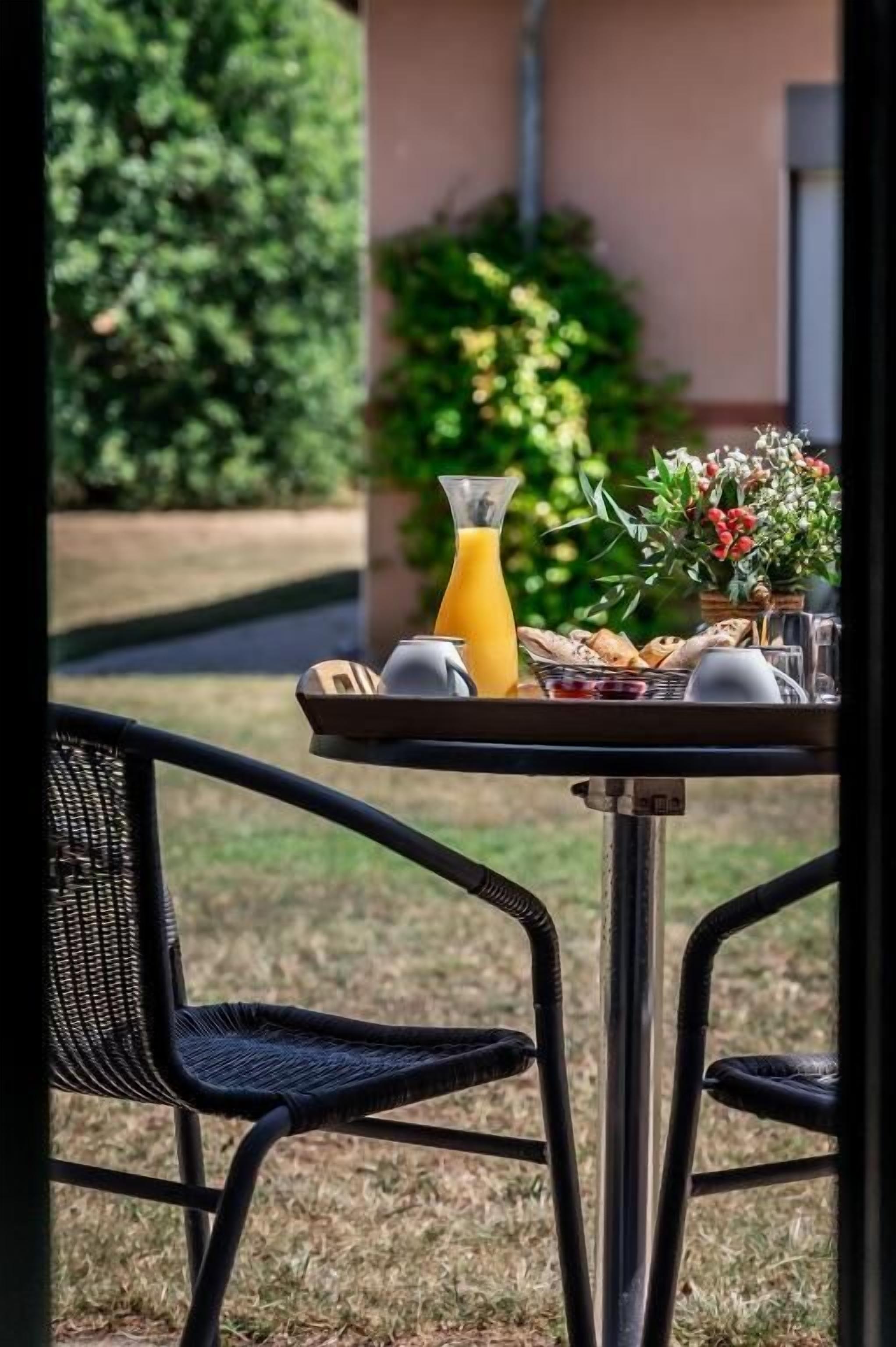 A table set outdoors with breakfast items including orange juice, pastries, and a vase of flowers.