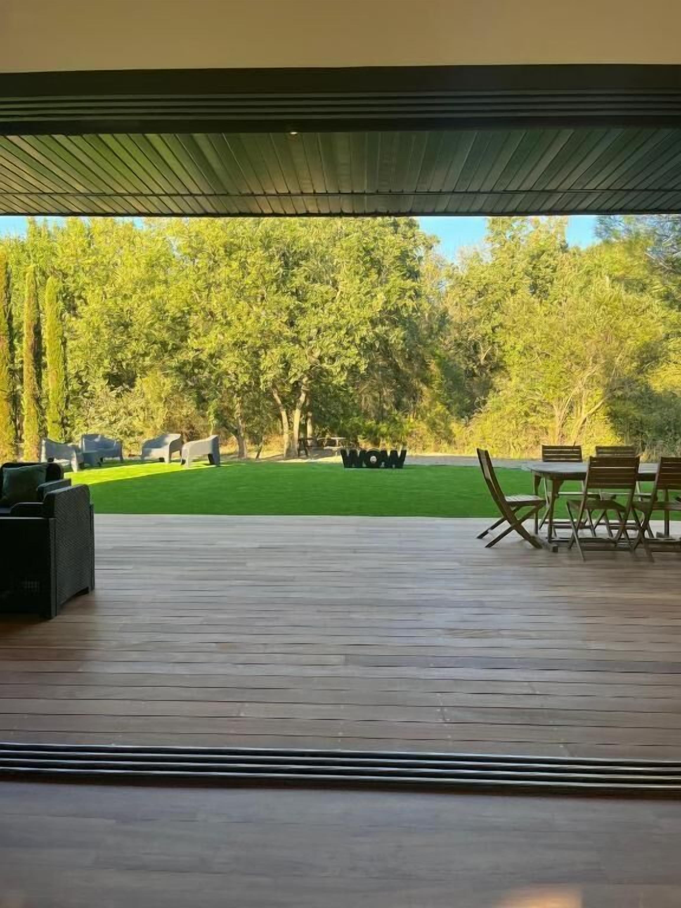 Une terrasse extérieure avec une plateforme en bois, un espace salon comprenant des chaises et une table, et une vue sur une pelouse verdoyante et des arbres.