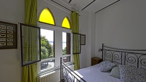 Un dormitorio con una cama, dos ventanas con cortinas verdes, un radiador y cuadros de mariposas en la pared.