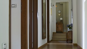 Un pasillo con suelo de madera, una puerta de madera, un espejo y un mueble con un jarrón de flores.