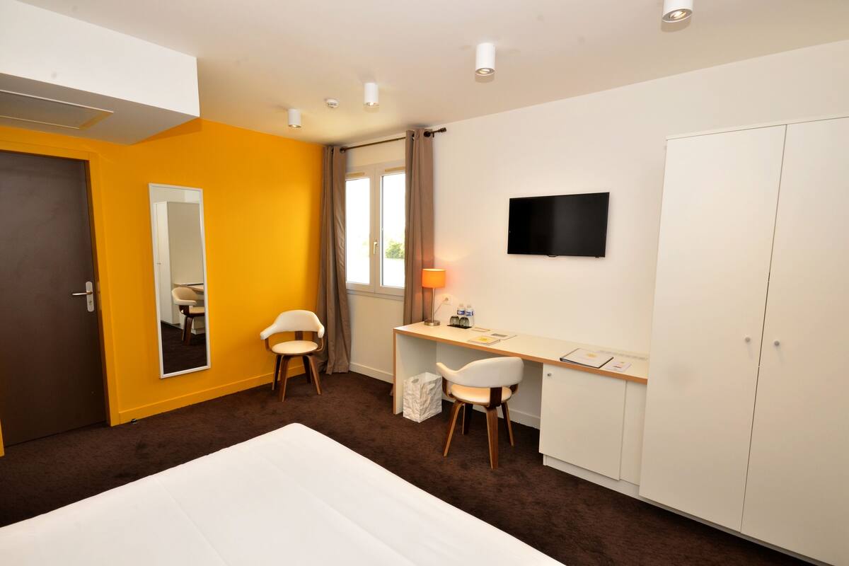 A hotel room with a bed, a desk, two chairs, a TV, and a wardrobe.