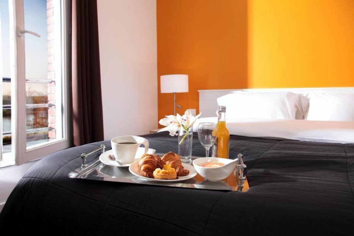 A hotel room with a bed, a tray with breakfast items, a window, and a lamp.