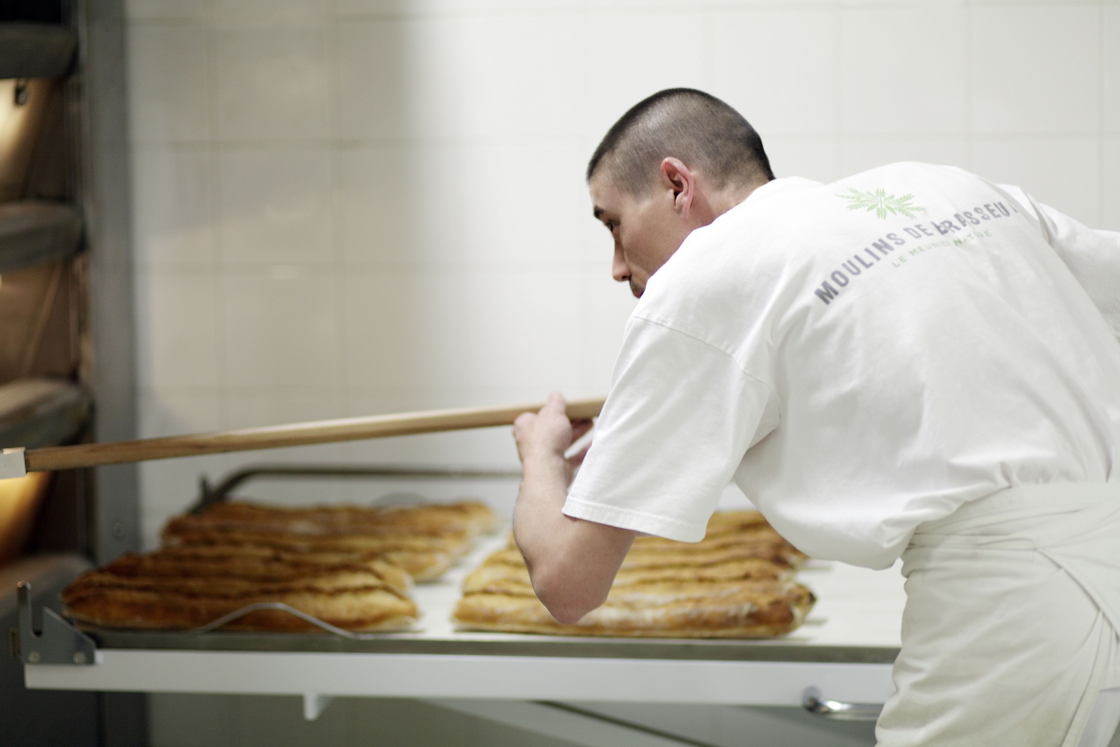 A person in a white uniform with text on the back, handling a large flatbread in a bakery setting.
