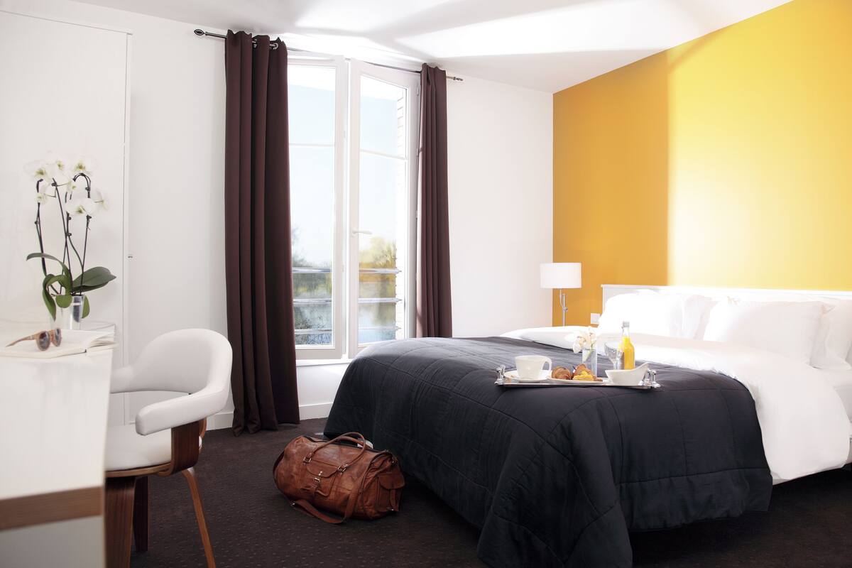 A hotel room with a bed, a desk, a chair, a window with curtains, and a view of the outside.