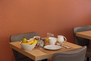 Una mesa de desayuno con un bol de fruta, un jarro de jugo, una taza blanca y un plato.