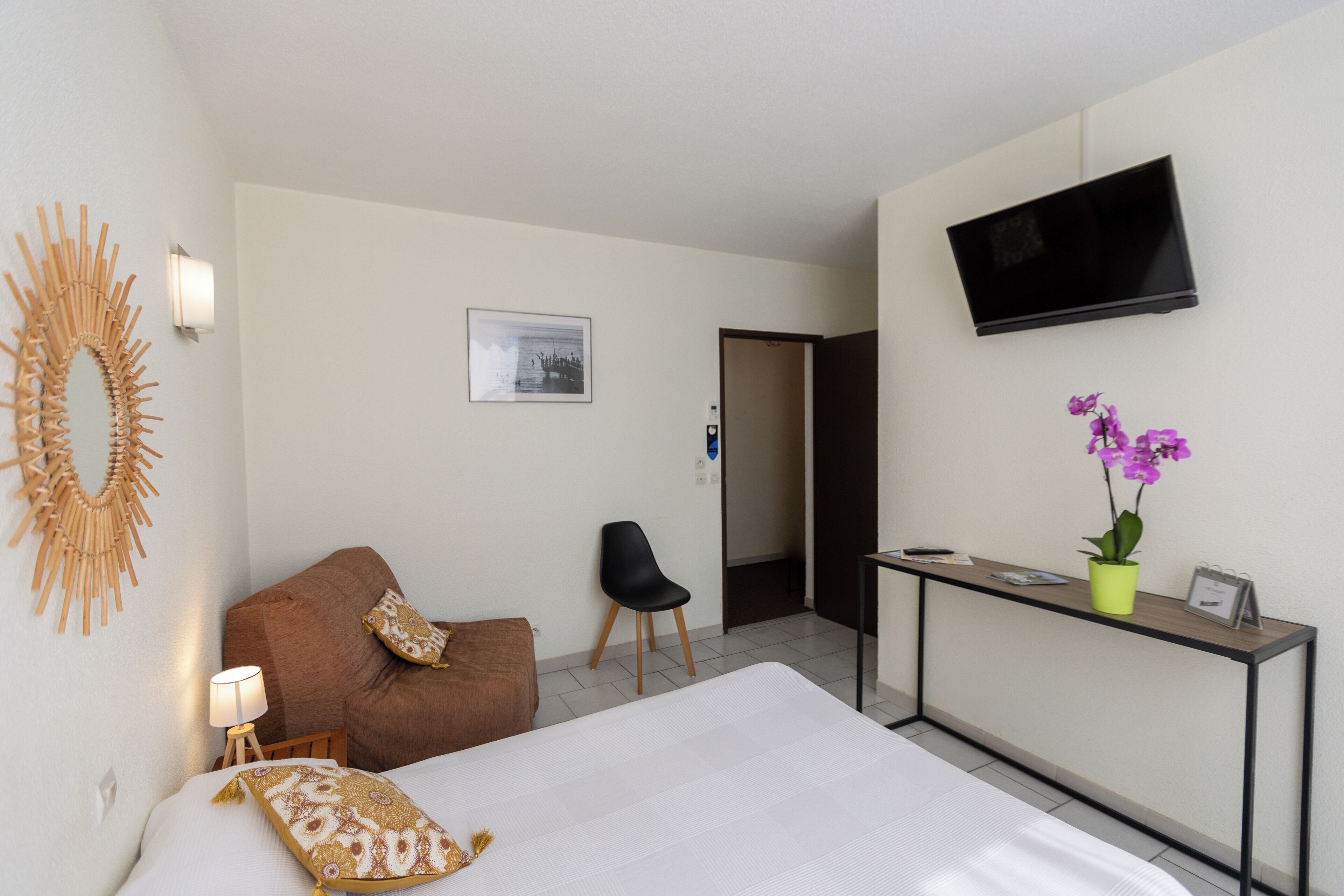 Habitación de hotel con cama, escritorio, televisor, silla, sofá, lámpara y un adorno en la pared.