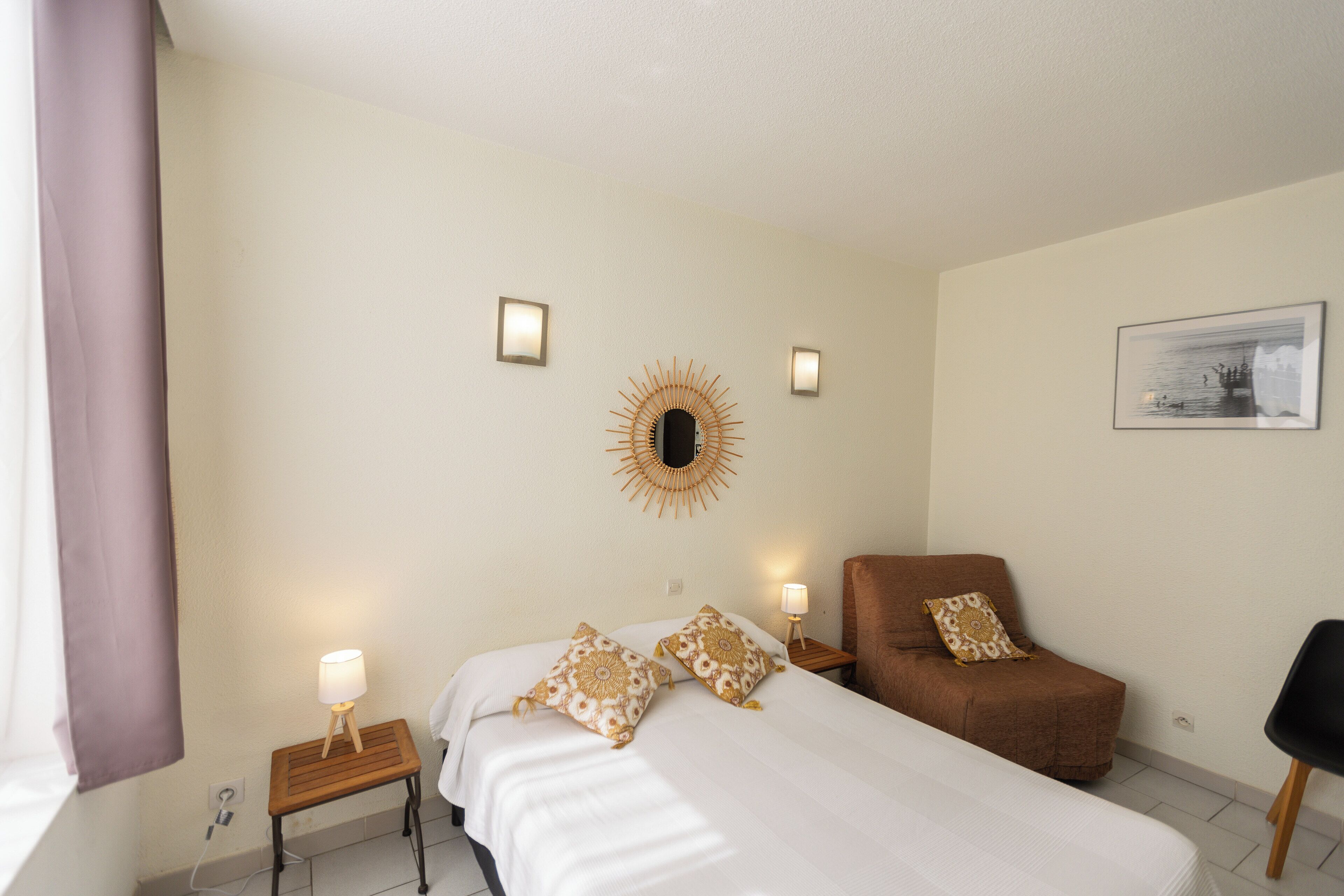 Ein Hotelzimmer mit einem Bett, einem Sessel, einem kleinen Tisch mit Lampe und einem wandmontierten Spiegel.