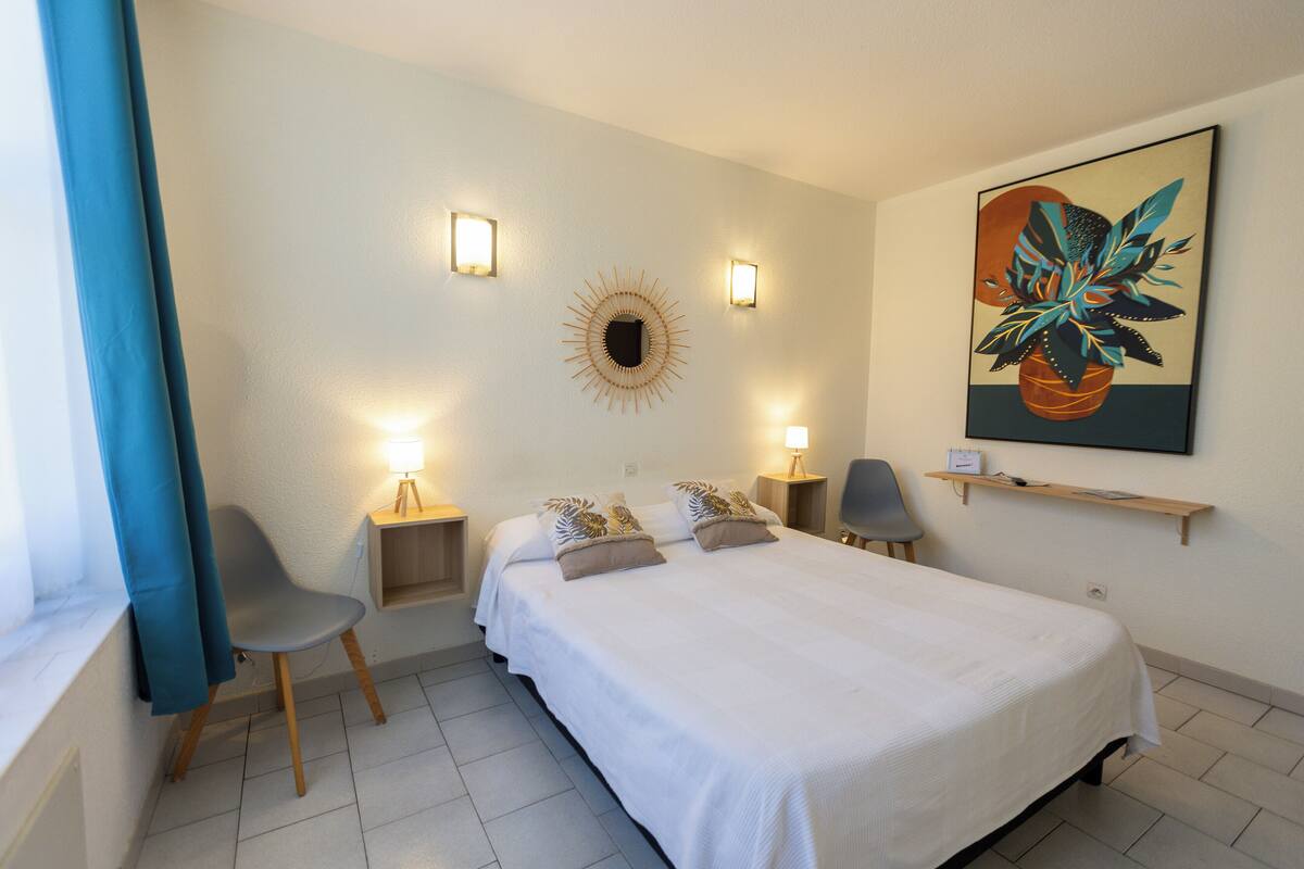 Un dormitorio con una cama grande, dos mesitas de noche, una silla, un estante en la pared y un cuadro.