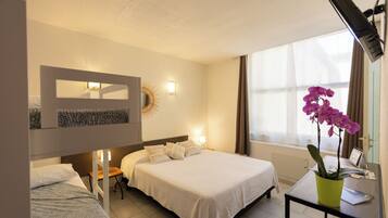 A hotel room with a large bed, a smaller bed, a desk with a plant, and a window with curtains.