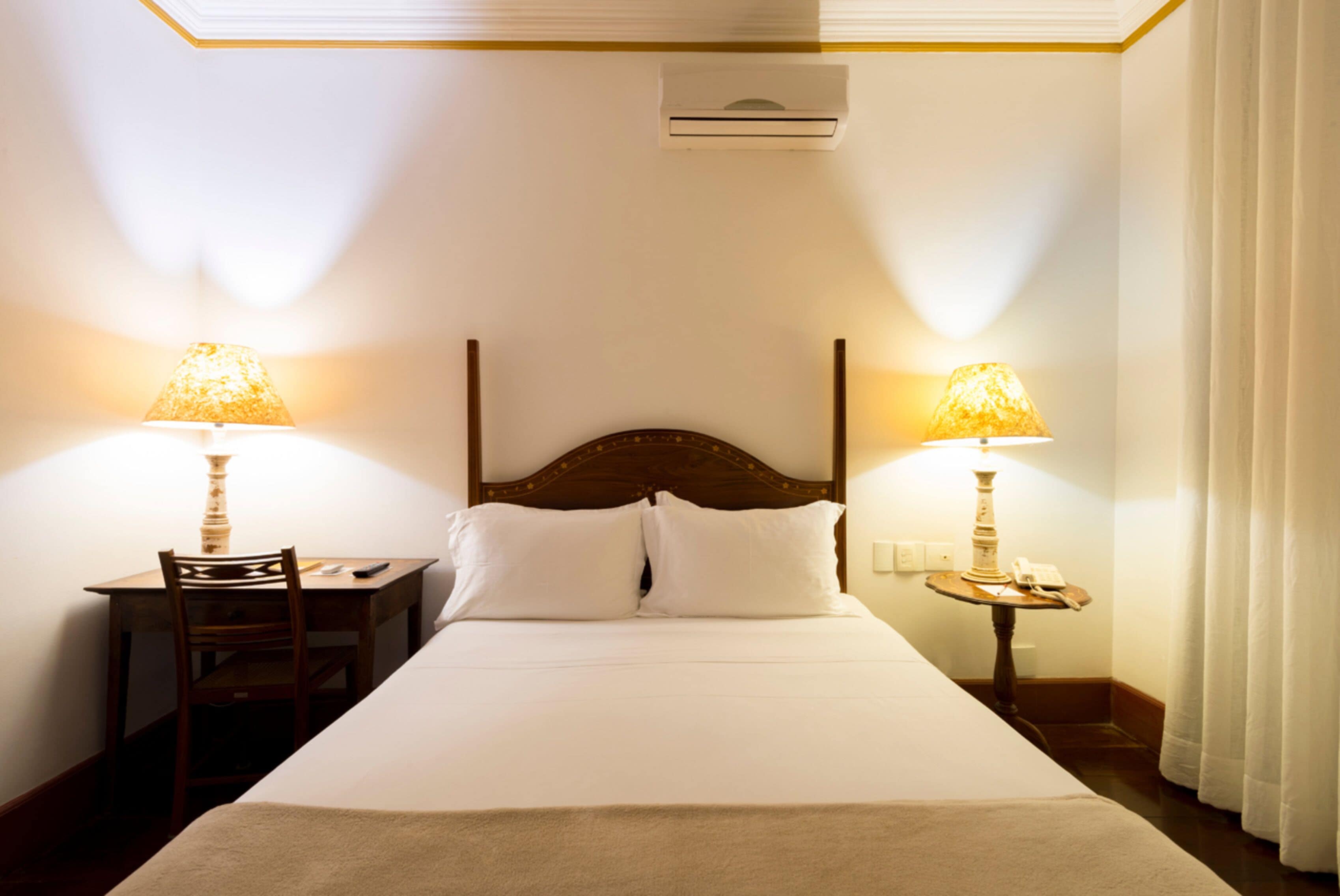 Habitación de hotel con una cama grande, dos lámparas de noche, un escritorio con una silla y un equipo de aire acondicionado en la pared.