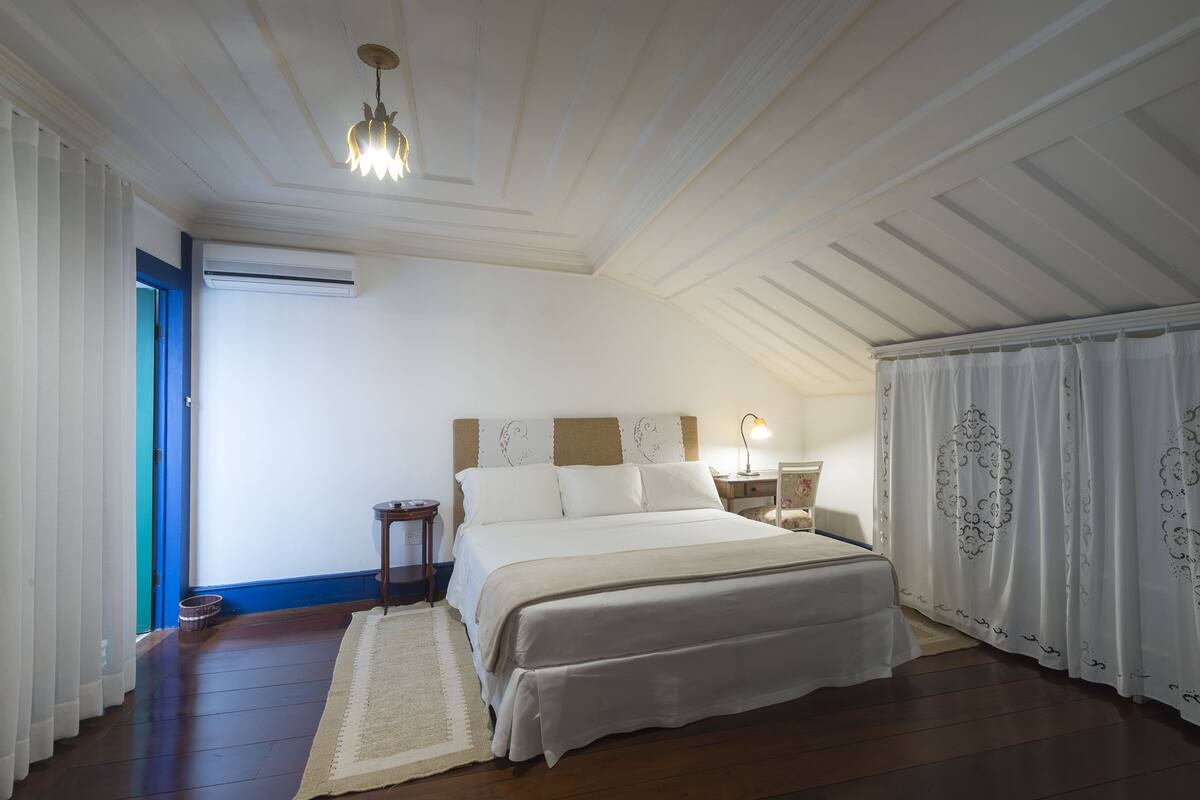 Un dormitorio con una cama grande, una mesita de noche, una lámpara y un ventanal con cortinas.