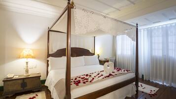 A four-poster bed with white linens and rose petals, a bedside lamp, and a wooden nightstand.