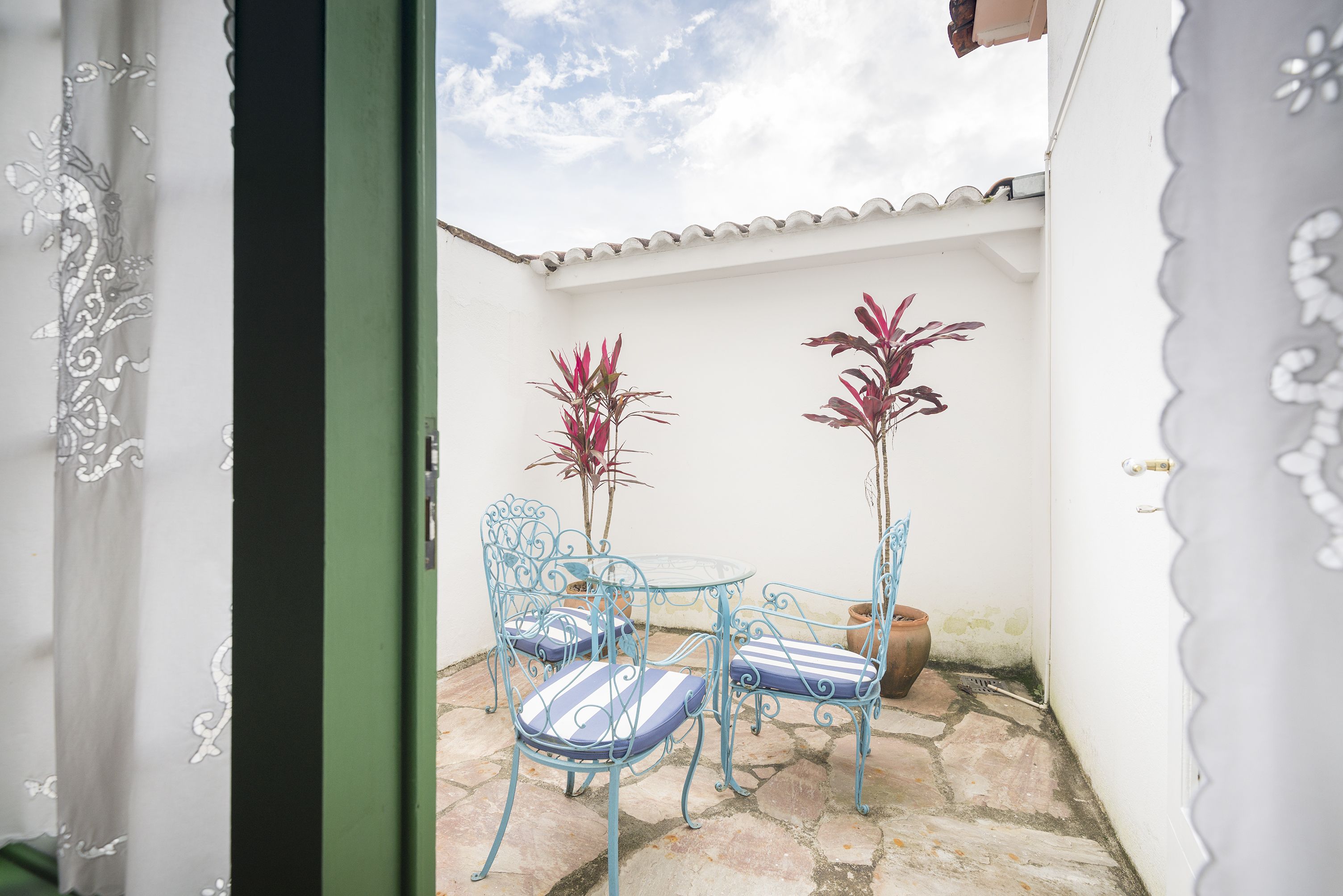A small outdoor patio with a table and chairs, potted plants, and a white wall.