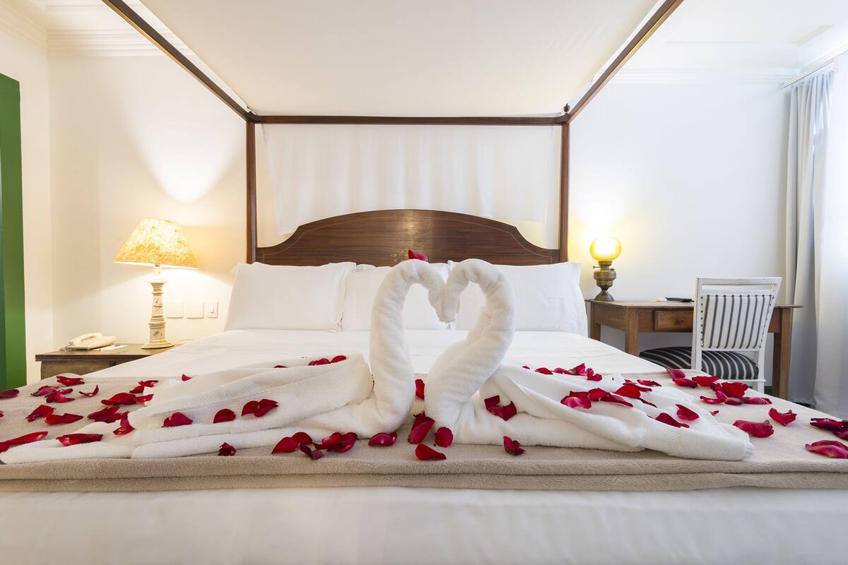 Habitación de hotel con una cama bien hecha, una lámpara de noche, una silla y una mesita de noche con teléfono.